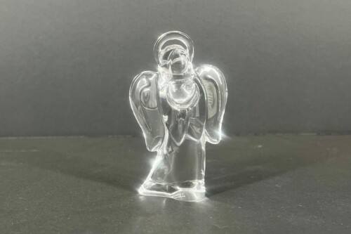 Clear glass angel figurine standing on a dark surface, wings spread and halo visible