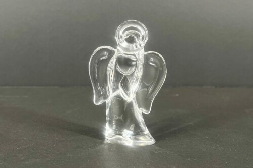 Crystal glass angel statue standing on a dark surface with wings extended outward.