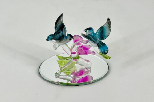 Glass sculpture of two blue birds facing a pink flower on a mirrored base.