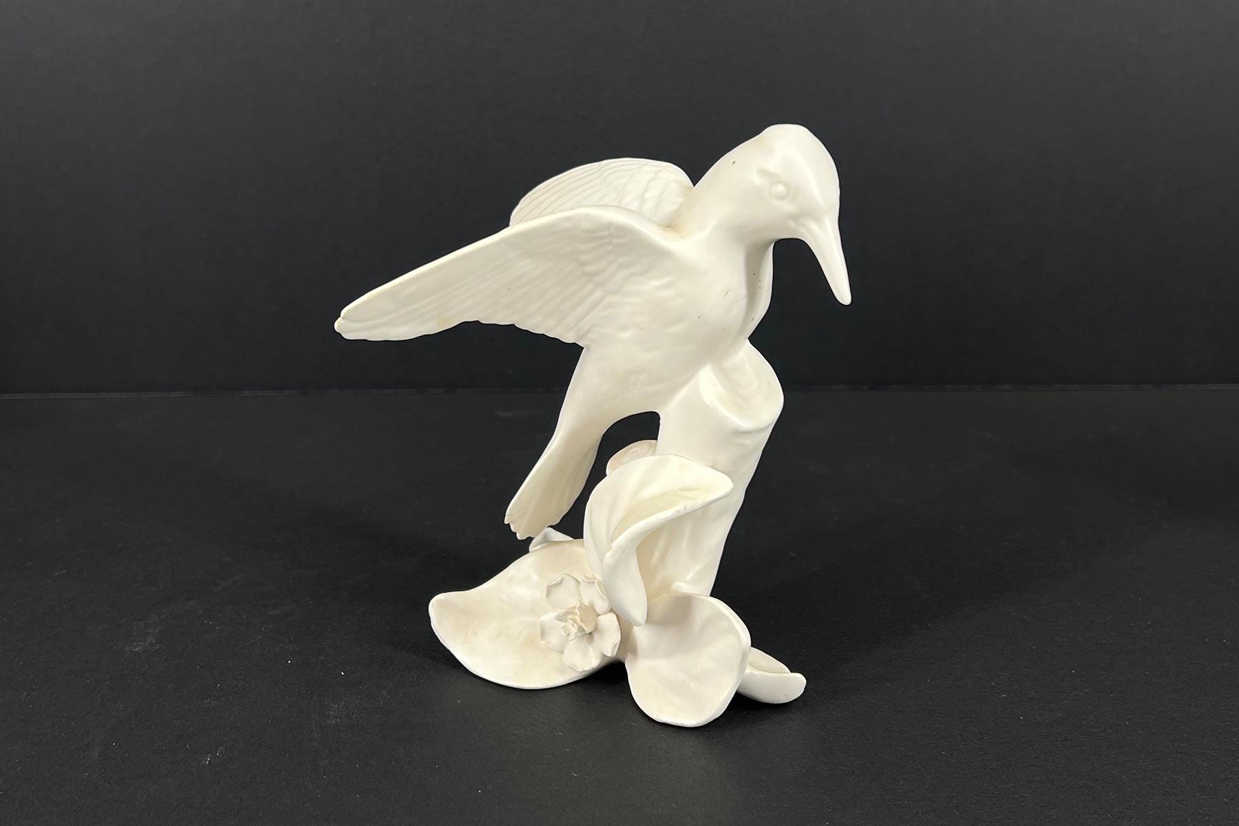 White ceramic sculpture of a bird with a long curved beak and outstretched wings on a floral base (decorative statue)