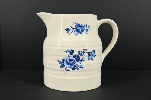 White ceramic pitcher with a blue floral pattern (roses and leaves) against a dark background.