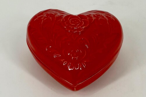 Glossy red heart-shaped box with embossed floral patterns on its lid, resting on a pale surface