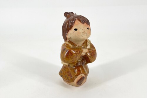 Ceramic figurine of a young child in brown robes, kneeling with hands pressed together in prayer.