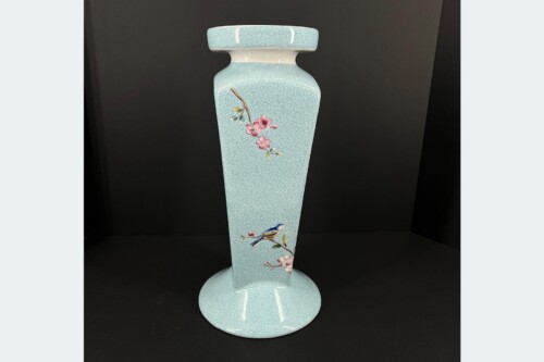 Tall pale blue crackle-glaze vase with a floral branch and small blue bird painted on it, set against a dark background