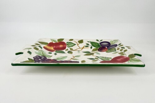 Decorative ceramic plate with a colorful fruit pattern (apples, grapes, plums) and green trim along the edge on a white background.