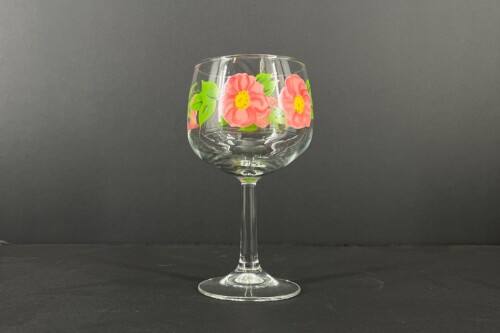 A clear stemmed glass with a pink floral pattern against a dark background, centered in view
