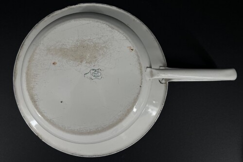 Top-down view of a white enamel pan/plate with a long handle on a black background, showing heavy scratches and rust stains.