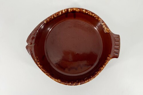 Top-down view of a round brown ceramic casserole dish with handles and a decorative chipped edge