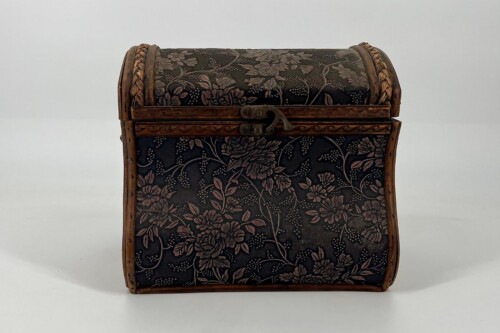 Antique wooden chest with a curved lid, dark floral fabric, and brass latch.