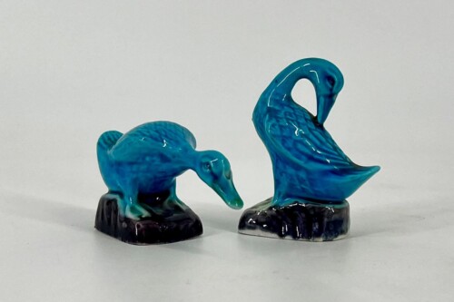 Two blue ceramic flamingo figurines with curved necks standing on dark bases on a light background.