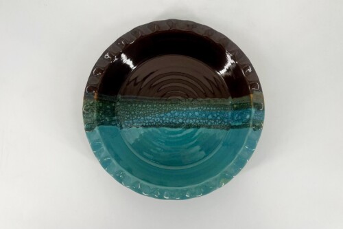 Round ceramic plate with teal glaze at the bottom fading to dark brown at the top, scalloped edge visible from above.