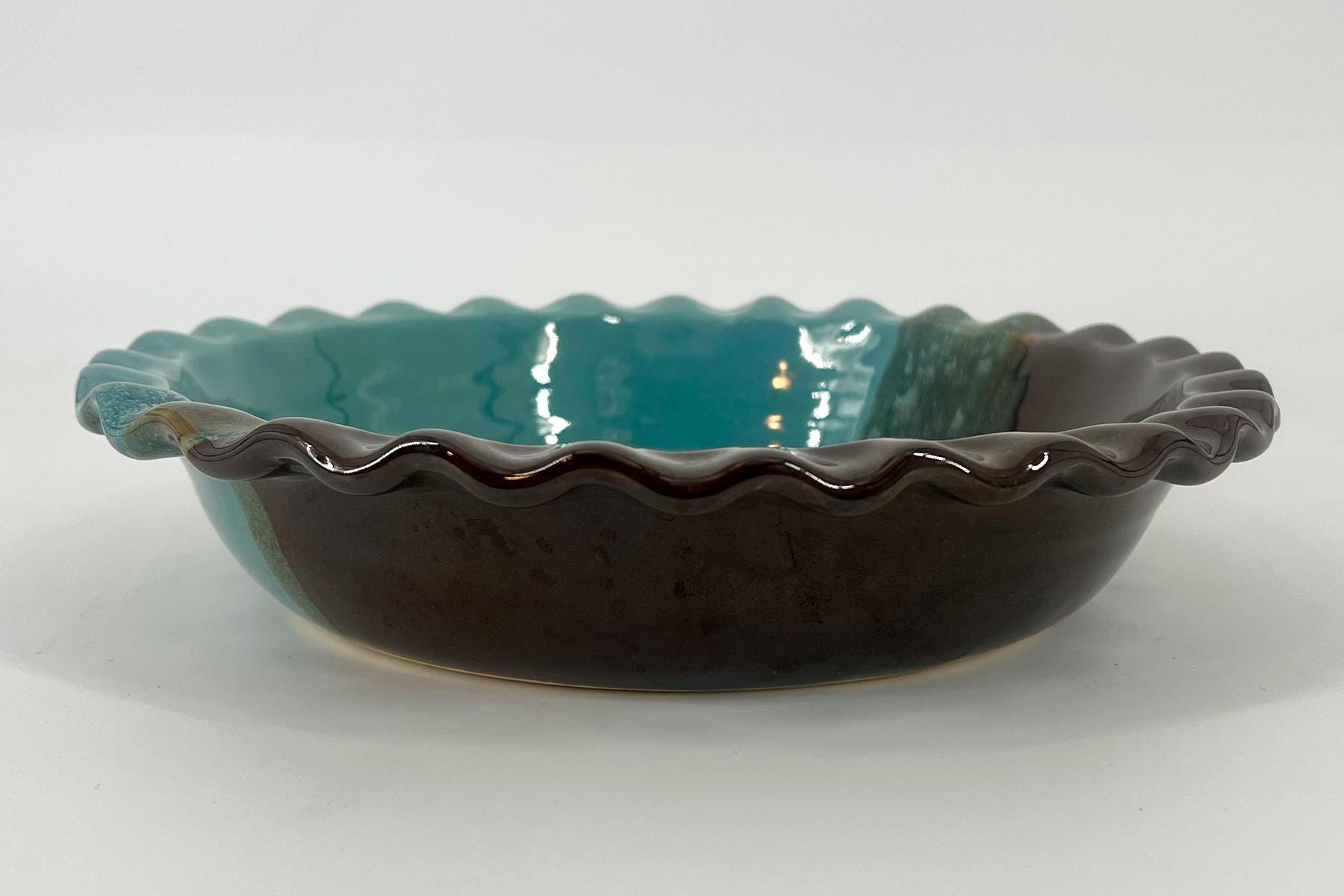 Ceramic bowl with a teal glossy interior and dark brown exterior, featuring a scalloped, wavy rim and shallow form.