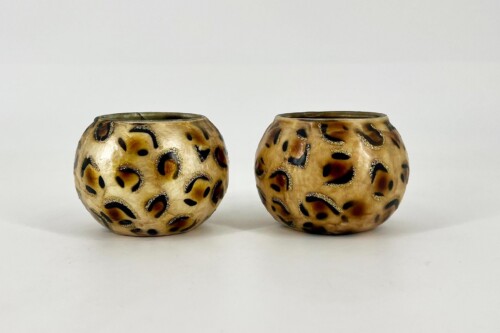 Two round leopard‑print ceramic vessels side by side on a white surface (gold, brown and black patterns).