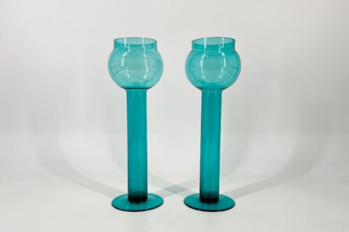 Two turquoise glass goblets with long stems, placed side by side on a white surface.