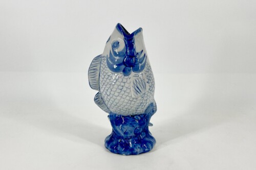 Blue-and-white glazed ceramic fish statue on a blue rocky base, facing upward.