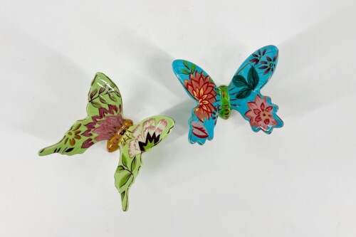 Two bright, floral-painted metal butterflies in lime green and turquoise hover against a pale background, looking decorative.