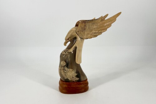 Carved wooden eagle sculpture with outstretched wings mounted on a round base, showing detailed feather carving.