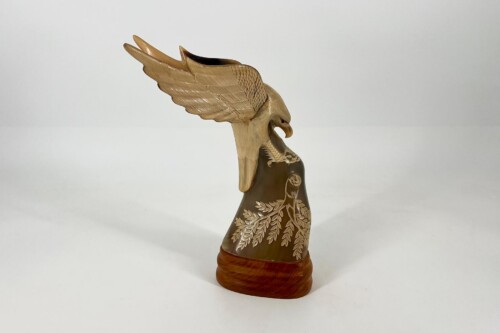 Wooden eagle sculpture with outstretched wings perched on a carved pedestal with leaf motifs, neutral background