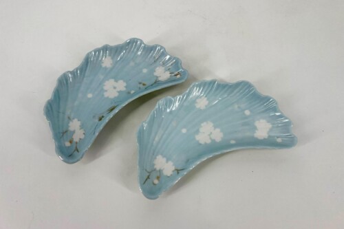 Two blue porcelain leaf-shaped plates with white cherry blossom patterns resting on a light surface (decorative dishware).