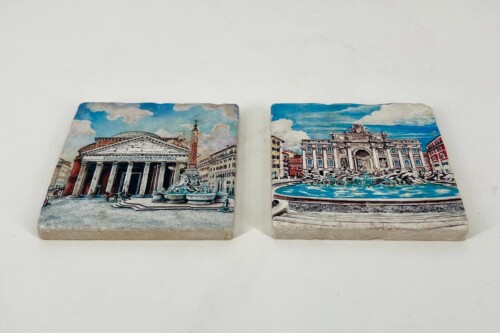 Two decorative tiles featuring European landmarks: left shows a domed, colonnaded building with an obelisk in front; right shows an ornate baroque fountain with statues and a blue sky.