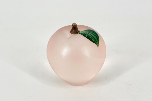 Decorative peach-shaped pink ball with a small brown stem and green leaf against a light background