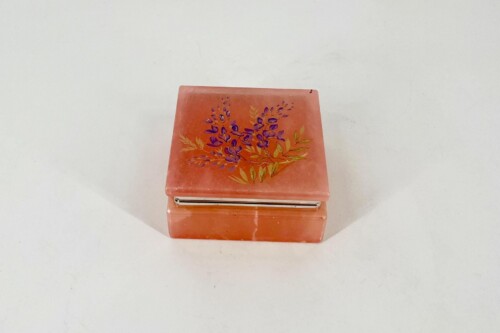Pink decorative jewelry box with purple floral design on a light background, closed atop a white surface