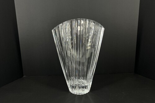 Clear cut crystal vase with vertical facets on a dark backdrop.