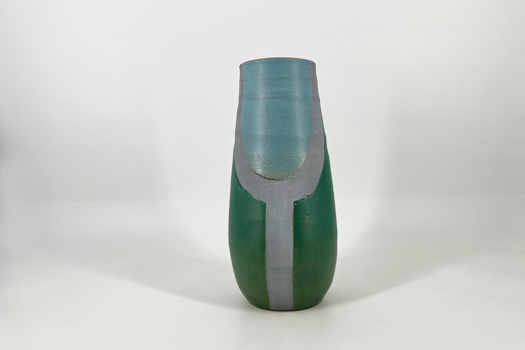 Close-up of a green bottle with a blue-tinted neck and a gray protective sleeve, showing a chipped rim at the top.