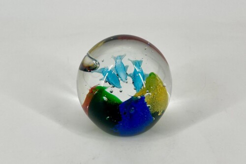 Clear glass marble containing blue, green, yellow, and red swirls, resting on a white surface.