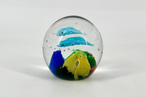 Clear glass marble containing bright blue, yellow, green, and red color swirls and bubbles, resting on a white surface.