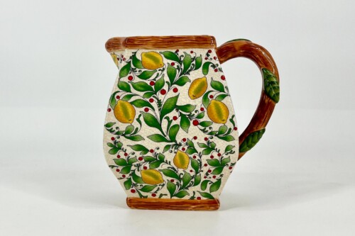 Ceramic pitcher with yellow lemons and green leaves in a crackled cream glaze, brown wooden handle and base.