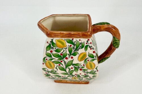 Ceramic pitcher with a lemon-and-leaf pattern, brown rim and branch-like handle.
