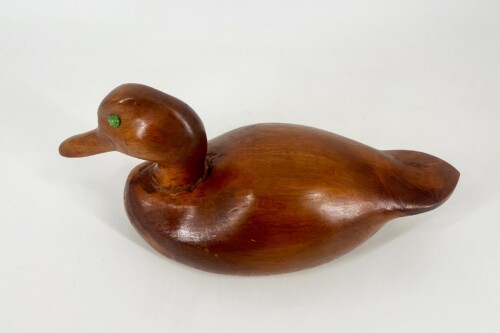 Hand-carved wooden duck decoy with a glossy brown finish and a small green eye viewed from the side.