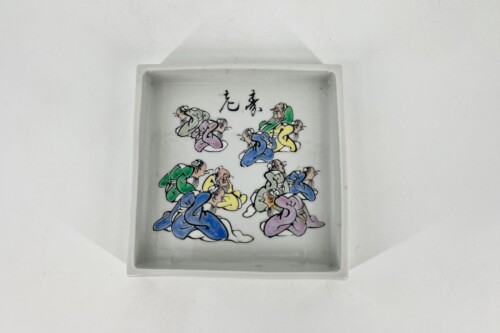 White rectangular ceramic tray with a colorful cartoon of kneeling, robed figures arranged in groups and Chinese characters above them.