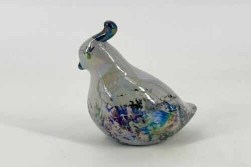Glass bird sculpture with an iridescent glaze and multicolored paint splatters on its body, facing left