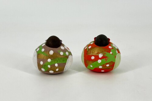 Two hand-painted Easter eggs with black tops sit on a white surface; one brown with green and white dots, the other orange with green and white dots.