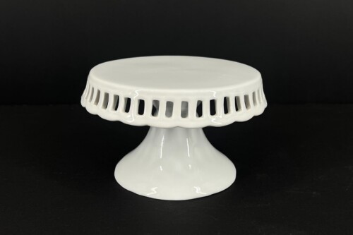 White ceramic cake stand with a glossy finish and round openwork edge on a black background.