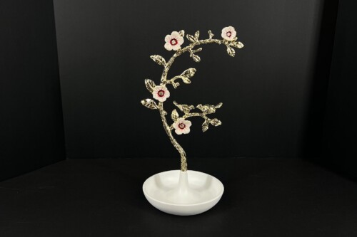 Gold-toned ornamental tree sculpture with white-pink flowers on a white pedestal against a black backdrop.