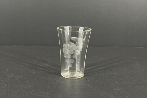 Clear glass tumbler filled with white round pills stacked inside against a dark surface.