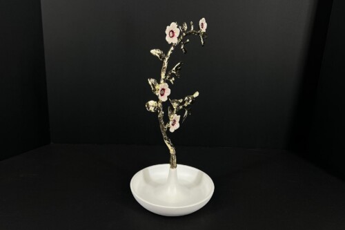 Gold-toned decorative flowering branch with pale pink centers, mounted on a white pedestal against a black background.