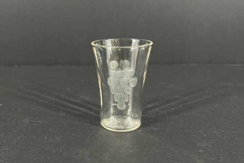 Clear shot glass on a dark surface containing a vertical stack of round coins or tokens against a black background