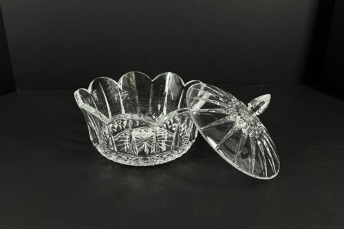 Clear cut-glass crystal bowl with a matching lid resting beside it on a black background.