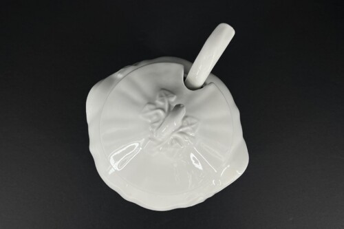 White ceramic circular dish with a tall cylindrical rod inserted through a cut in the rim, set against a black background.