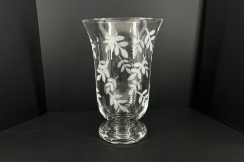 Tall clear glass vase with frosted leaf pattern on a black backdrop, standing on a surface.