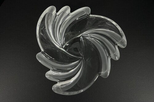 Abstract clear glass sculpture with swirling petal-like curves on a dark background, resembling a spiral flower.