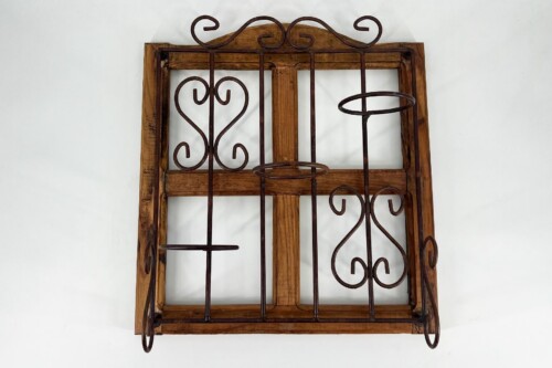 Rusty wrought-iron decorative grille with scroll patterns attached to a weathered wooden window frame against a white wall
