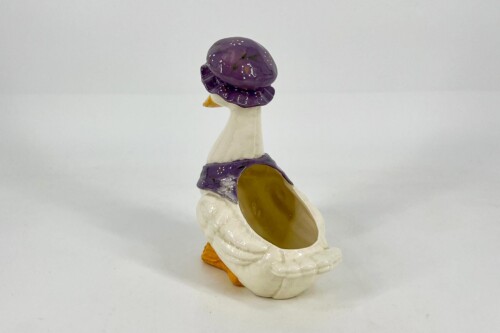 Whimsical ceramic sculpture of a white bird with a purple mushroom-shaped hat and a hollow body opening on the side.