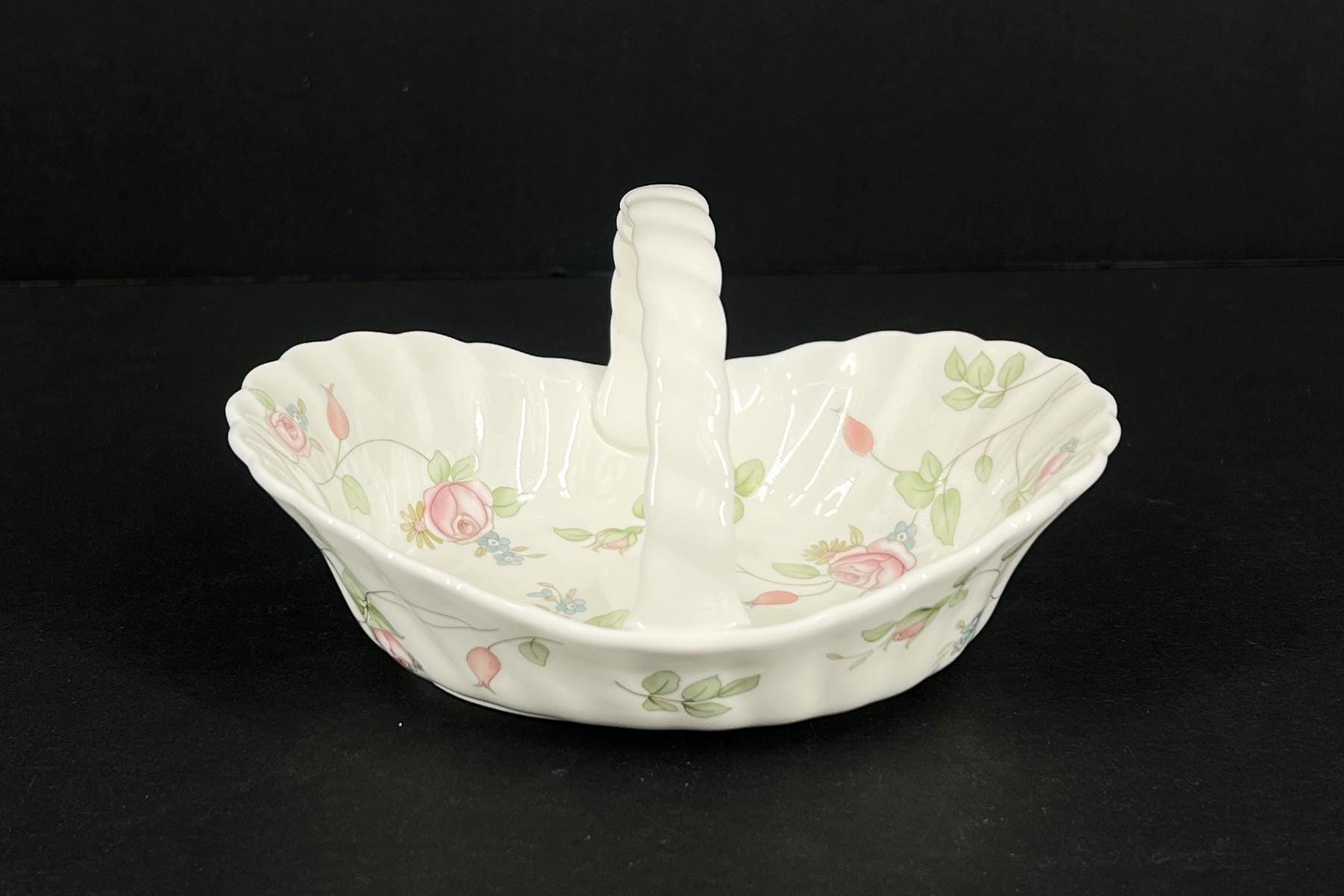 White porcelain dish with a floral pattern (pink roses, green leaves) and a tall central handle, set against a black background.
