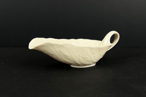 White ceramic gravy boat with a fluted, wavy rim and a curved handle on the right, glossy finish against a black background.