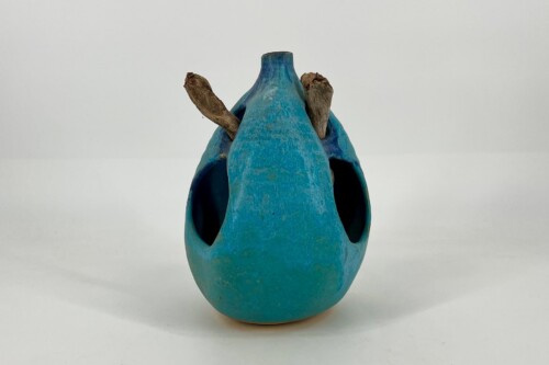 Blue ceramic vase with two dried, brown stems protruding from its sides, sitting on a white surface.